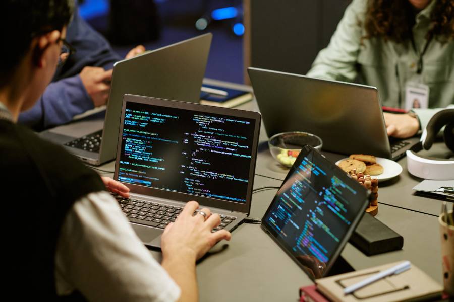 Desenvolvedores em reunião com laptops exibindo código, representando o processo de engenharia de software com IA. 